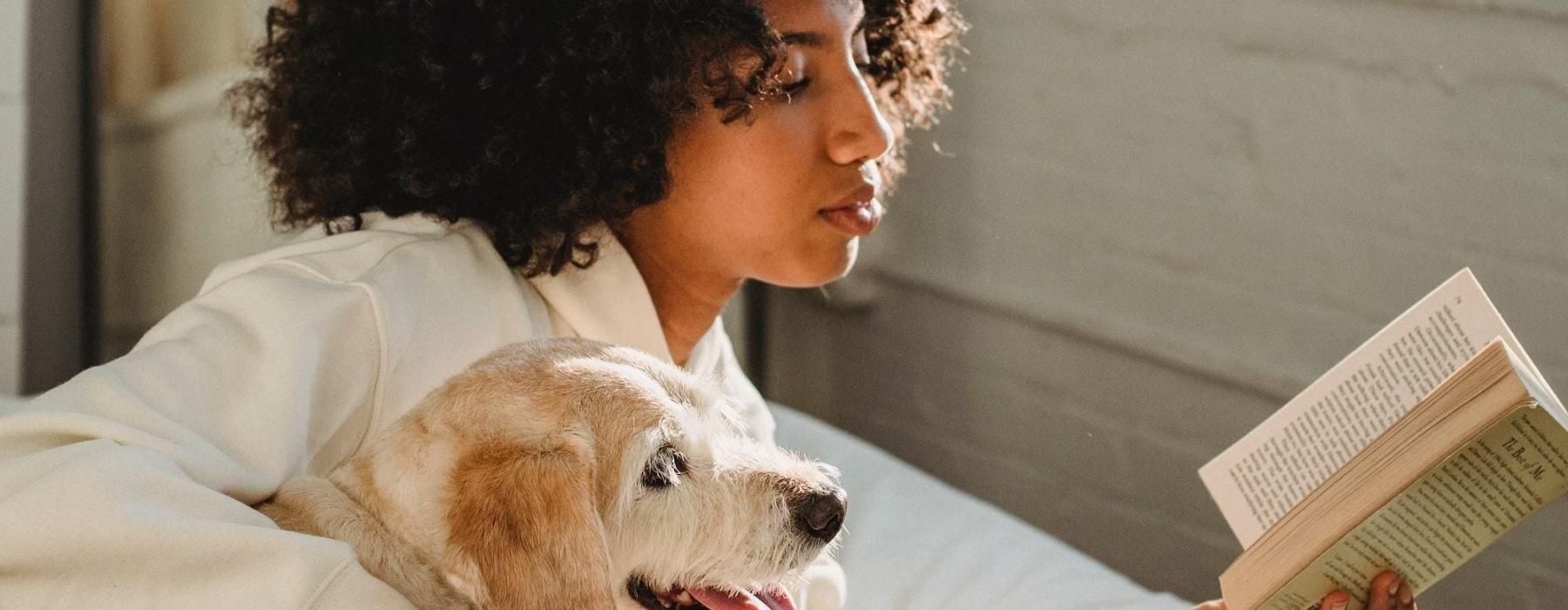 a person reading a book while laying next to a dog