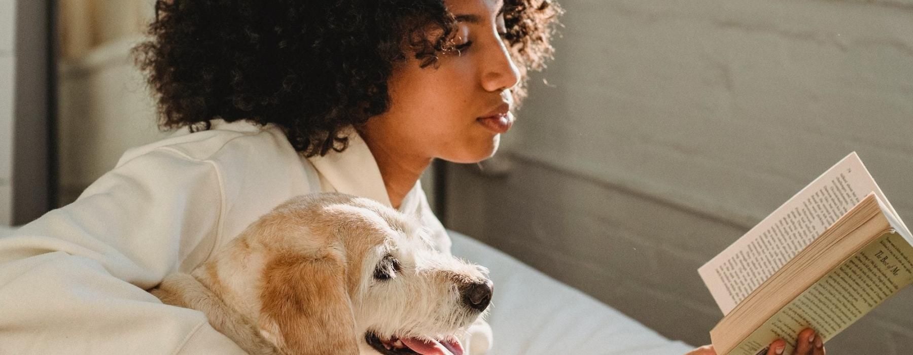 a person reading a book while laying next to a dog
